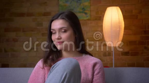 一位年轻美丽的白种人白种人女性在舒适的沙发上坐着看着摄像机微笑着拍摄特写镜头视频的预览图