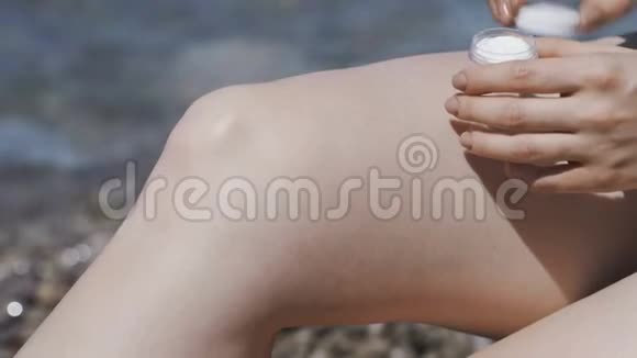 防晒霜一个女孩在海滩上用奶油涂抹腿部视频的预览图