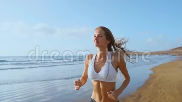 美丽的女人穿着运动短裤和t恤在海滩上奔跑沙滩上有白色的沙子和蓝色的海水视频的预览图