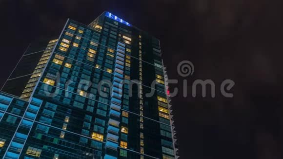 夜空云层高于现代摩天大楼明亮的窗户建筑时间推移视频的预览图