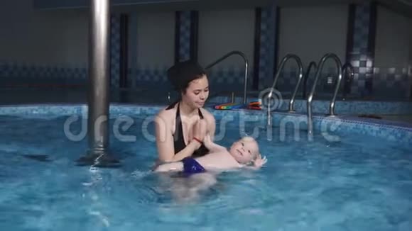 一位年轻的母亲教她的小儿子在游泳池里游泳游泳训练视频的预览图