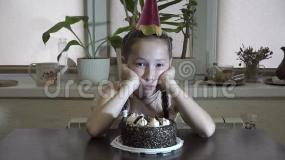 悲伤的小女孩坐在桌子旁头顶着双手头上戴着节日的帽子看着视频的预览图