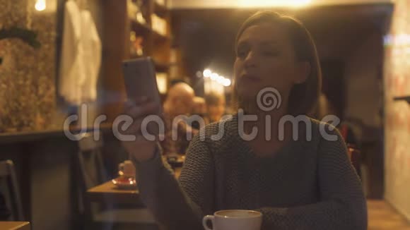 年轻女子在智能手机上聊天坐在舒适的咖啡屋里免费无线上网视频的预览图