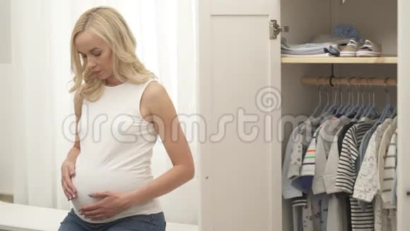 一个优雅的怀孕金发女郎用双手抚摸她的腹部她看着相机开心地笑着看着视频的预览图