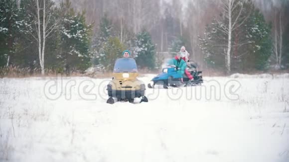 穿着五颜六色衣服的年轻人在冬天的森林里骑着雪地摩托慢动作视频的预览图