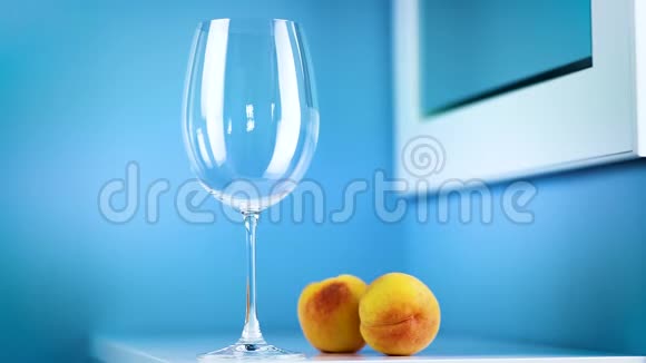 一杯蓝色背景的白葡萄酒正站在一张有两个桃子的白色桌子上视频的预览图