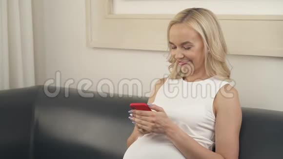 特写一位孕妇坐在沙发上手里拿着电话她看着屏幕微笑着视频的预览图