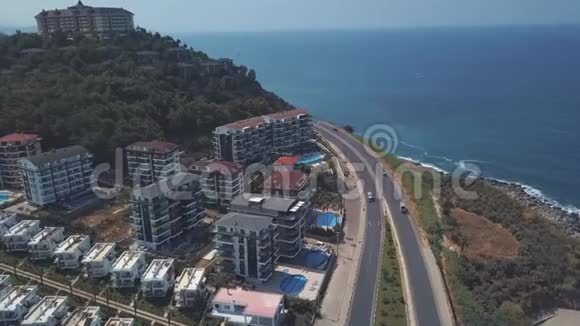 在温暖的夏日里在靠近大海的道路上行驶的汽车和站在斜坡上的豪华酒店的空中景观剪辑视频的预览图