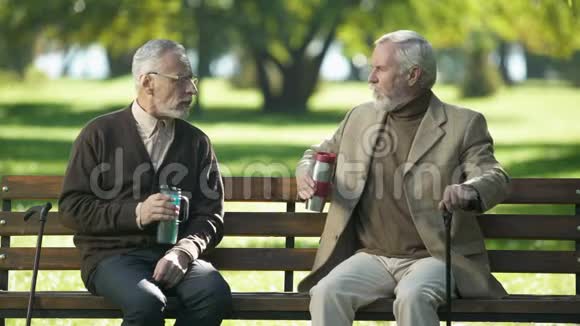 老人享受热茶坐在户外长凳上退休视频的预览图