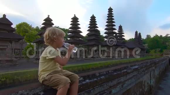 一个小男孩坐在塔曼阿云庙的墙上喝着塑料瓶里的水视频的预览图
