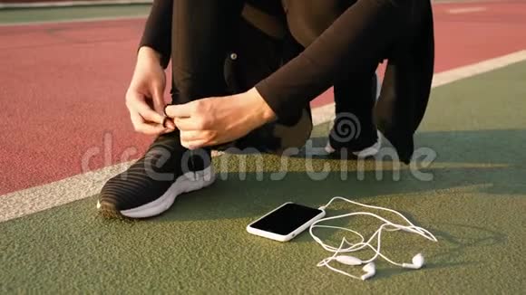 年轻的运动员女人把跑鞋和耳机绑在地上关门视频的预览图