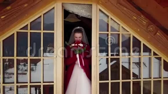 无人机的镜头从美丽的新娘身上飞过她站在木屋的阁楼上露出了那座山视频的预览图
