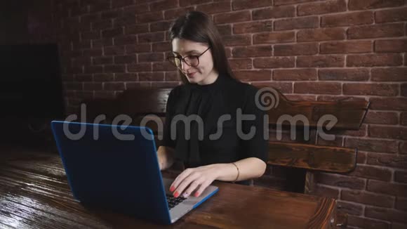 时尚的白种人年轻商务女性使用笔记本电脑坐在时髦的办公室红砖内部的桌子上女孩视频的预览图