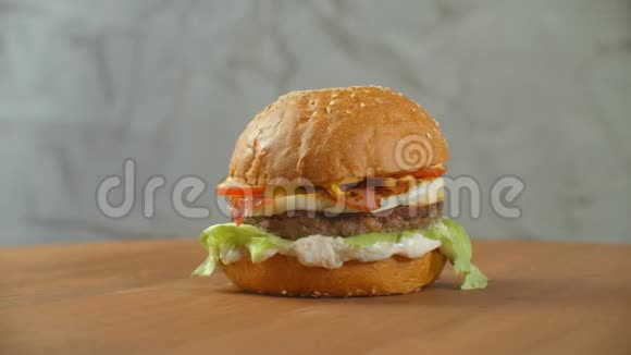 汉堡包在木板上旋转一个汉堡和一个切丁色拉奶酪和西红柿围绕着一个灰色的视频的预览图