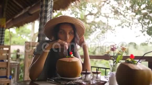 吸引人的年轻旅游少女在餐厅享用新鲜的椰子水鸡尾酒有美丽的热带丛林视频的预览图
