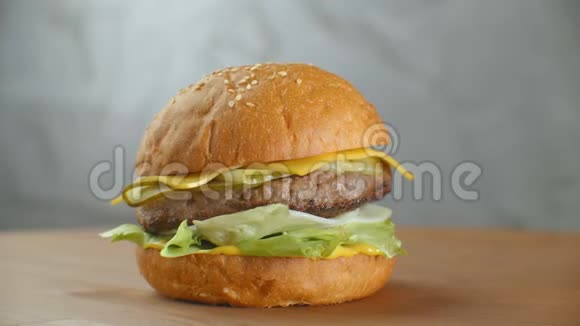 汉堡包在木板上旋转一个汉堡和一个切丁色拉奶酪和西红柿围绕着一个灰色的视频的预览图