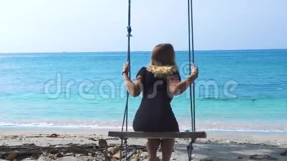 在海边荡秋千的快乐女人暑假期间年轻女孩在海滩秋千上摇摆在夏天玩得开心视频的预览图