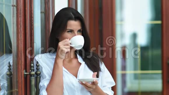 美丽的微笑女人在户外休息时手拿着热咖啡或茶手拿着杯子和茶碟视频的预览图