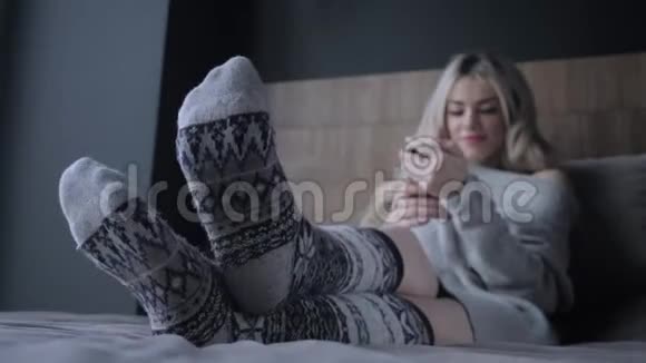 脚上的特写和针织袜子美丽的金发女人坐在床上带着智能手机博客视频的预览图