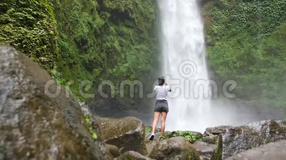 年轻的旅行者女孩使用手机拍摄惊人的丛林瀑布在巴厘岛印度尼西亚4K慢镜头电影视频的预览图