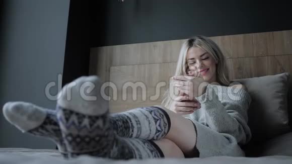 脚上的特写和针织袜子美丽的金发女人坐在床上带着智能手机博客视频的预览图