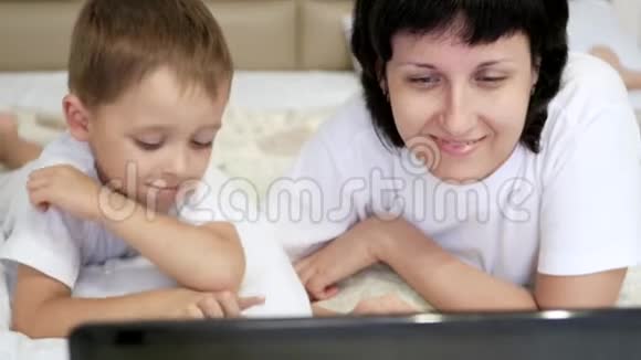 幸福家庭妈妈和孩子正躺在床上开心地看着笔记本电脑屏幕视频的预览图