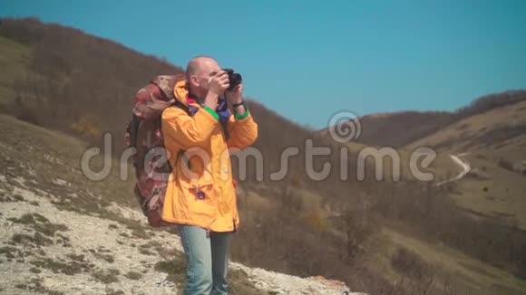 一个穿着黄色夹克和眼镜的人站在山上欣赏风景在dslr相机上拍照视频的预览图