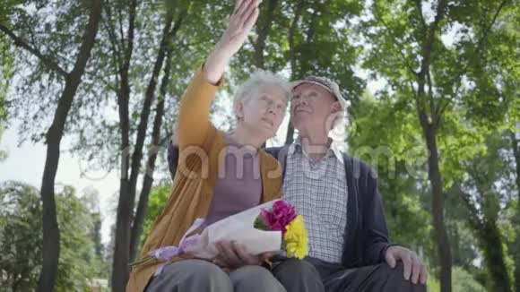 一对恋爱中的成熟夫妇坐在公园的长凳上的肖像成年女子手捧一束美丽的鲜花视频的预览图
