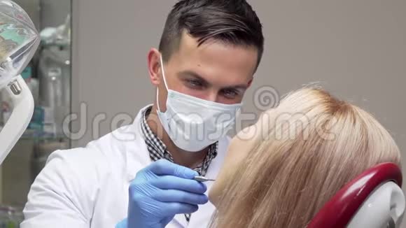 戴着医疗面具的开朗牙医在检查病人牙齿时大笑视频的预览图