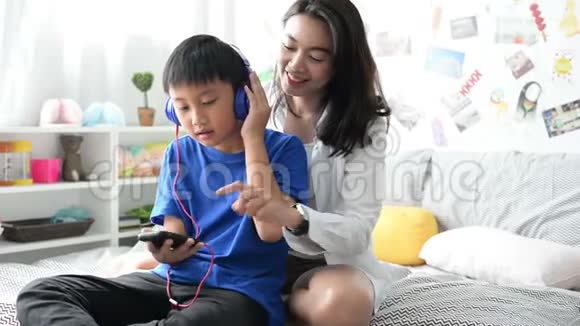 母亲和儿子戴着耳机用智能手机在家里一起听音乐视频的预览图