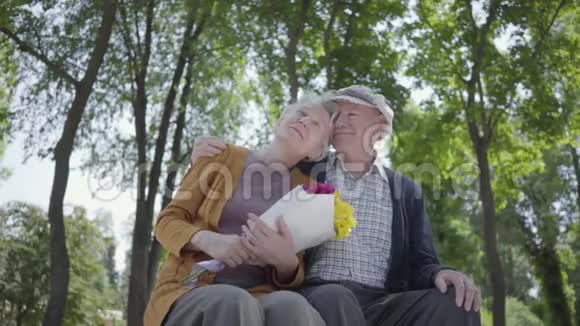 一对恋爱中的成熟夫妇坐在公园的长凳上的肖像成年女子手捧一束美丽的鲜花视频的预览图