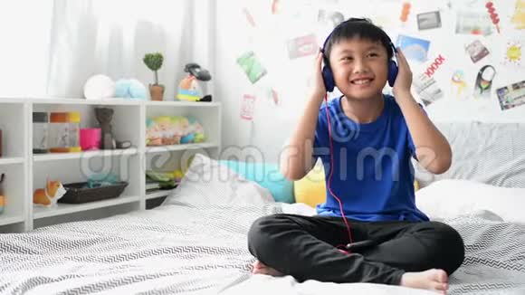 带耳机的小亚洲男孩用小玩意听最喜欢的音乐视频的预览图