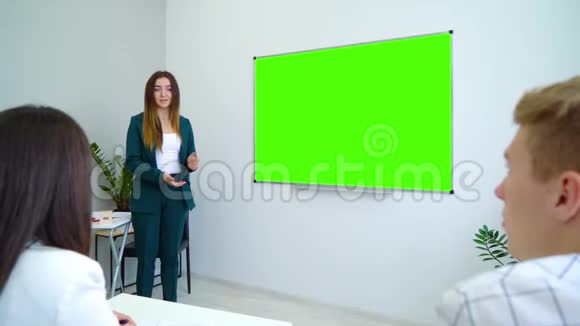 年轻快乐的老师旁边有一块绿色的屏幕板在教室里教学生视频的预览图