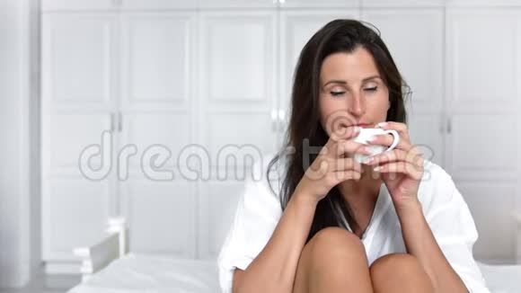 中镜头快乐微笑的女人在床上喝茶或咖啡享受美妙的早晨视频的预览图