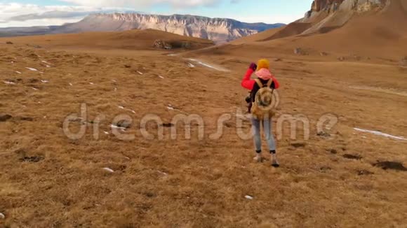 空中景色一个旅行女孩脖子上戴着相机正沿着山坡走着一片群山和一个背景视频的预览图