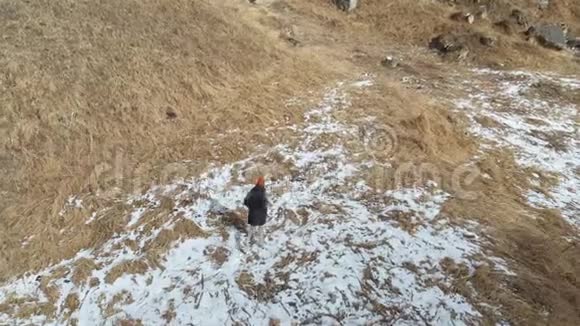 初冬穿着羽绒服和帽子的女游客沿着小径散步一片阳光明媚的草地和一片片雪视频的预览图