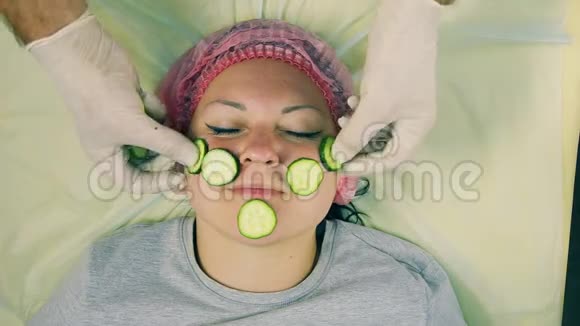 一个戴手套的男性美容师的手在女人脸上黄瓜碎片视频的预览图