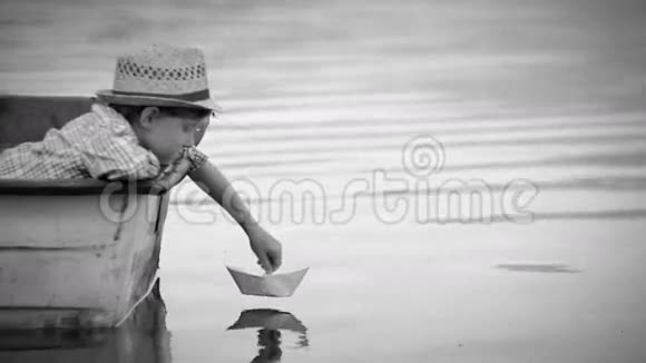 黑白镜头小男孩在坐在渔船上的旅途中送出一艘手工纸船视频的预览图