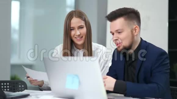 男性和女性微笑的同事讨论使用笔记本电脑坐在现代办公室的视频的预览图