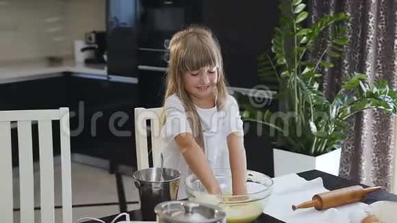 微笑的小女孩在厨房里的一大杯碗里揉一个面团厨房里快乐的小女孩孩子视频的预览图