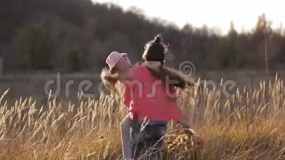 两个快乐的姐妹在田野的中央在温暖的夕阳的照耀下在草地上旋转视频的预览图