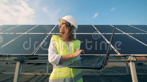 有魅力的女专家站在一个巨大的太阳能电池前操作笔记本电脑视频的预览图