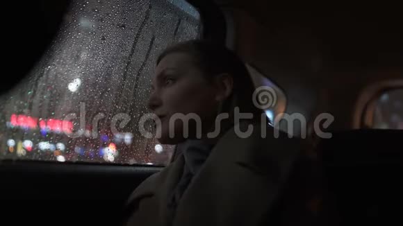 悲伤的女人晚上乘出租车在雨中看着车窗城市的灯光视频的预览图