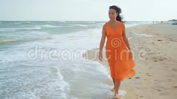 穿着橙色衣服的漂亮女人穿过海边沙滩沉思地向前看视频的预览图