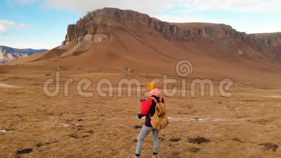 空中景色一个旅行女孩脖子上戴着相机正沿着山坡走着一片群山和一个背景视频的预览图