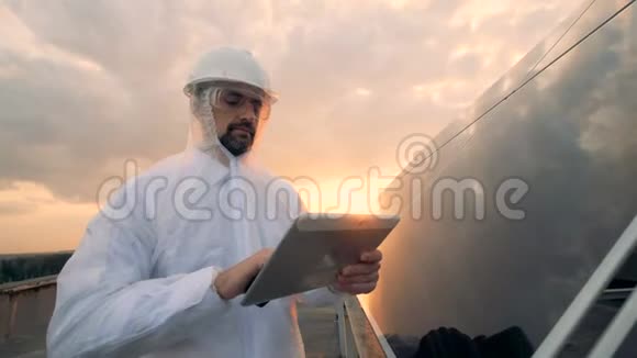日落的天空和一位装备精良的能源专家站在太阳能电池板附近视频的预览图
