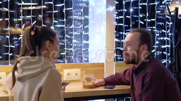一对夫妇坐在咖啡馆里聊天喝咖啡看智能手机视频的预览图
