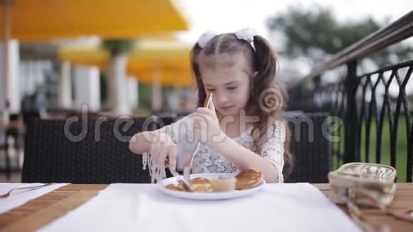 一个吃午饭的小女孩的肖像小女孩在街头咖啡馆里学着用刀叉吃饭视频的预览图