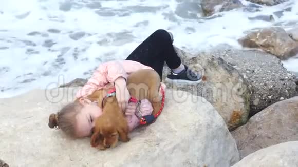 小女孩和她可爱的小狗躺在岩石上视频的预览图