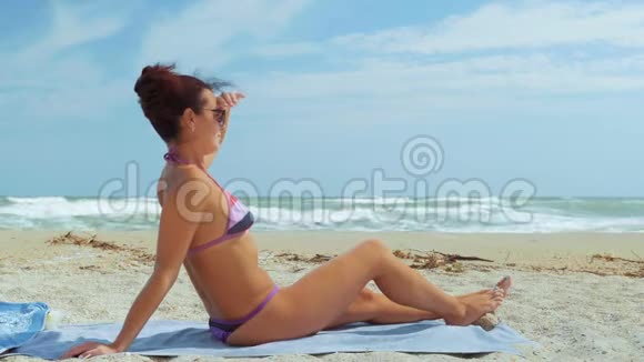 美丽的女人穿着泳衣和太阳镜坐在海边向前看视频的预览图